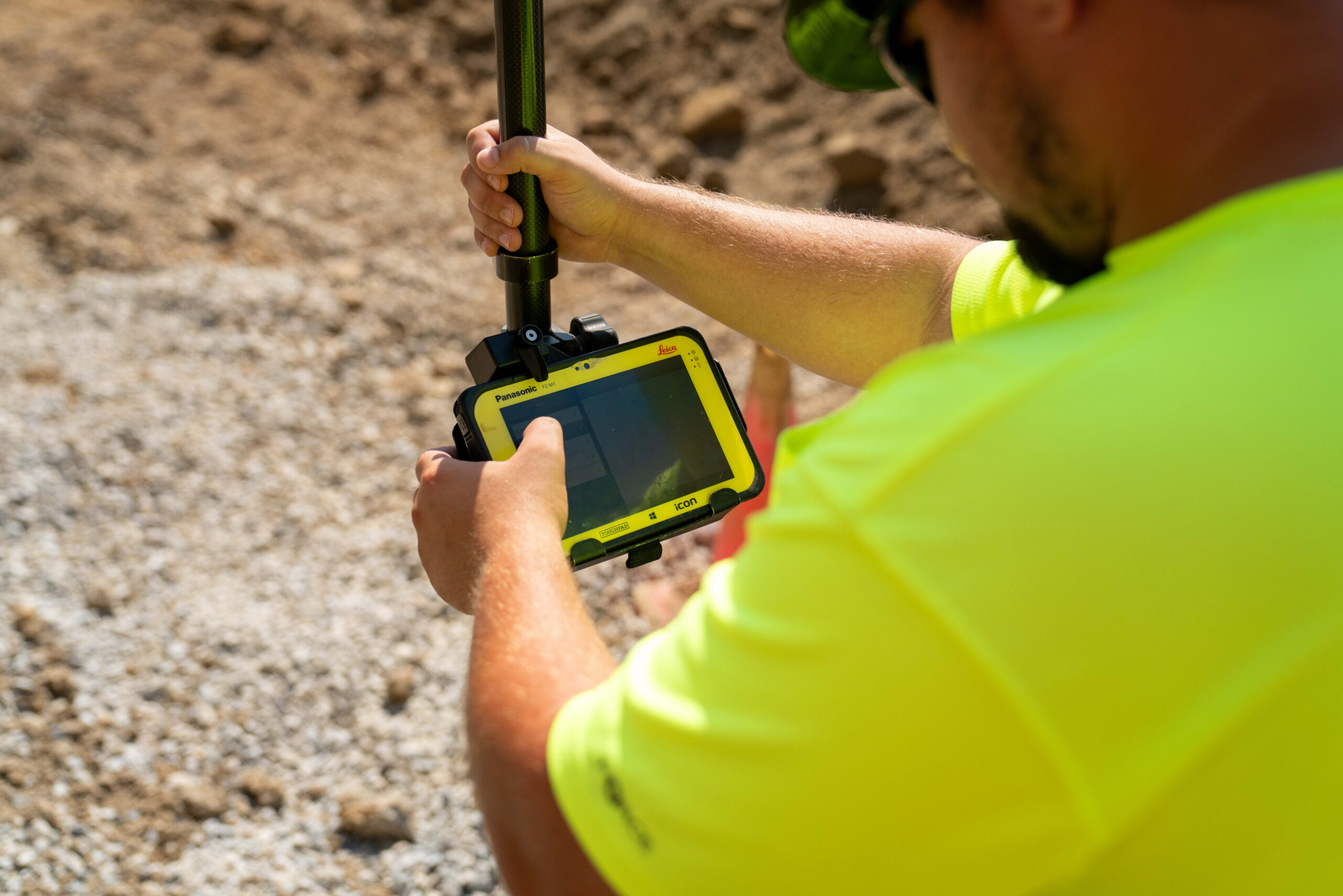 Person in neon yellow shirt uses device at gravel site.