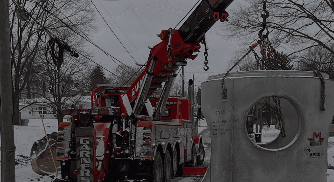 Red crane truck lifts concrete structure with circular opening in snow.