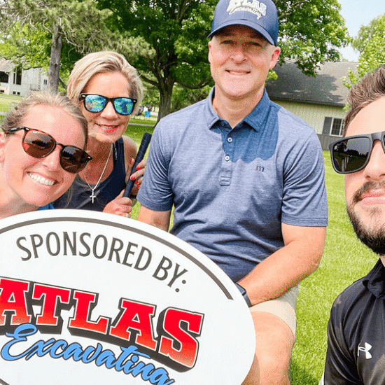 Four adults by Atlas Excavating sign, outdoors with trees.