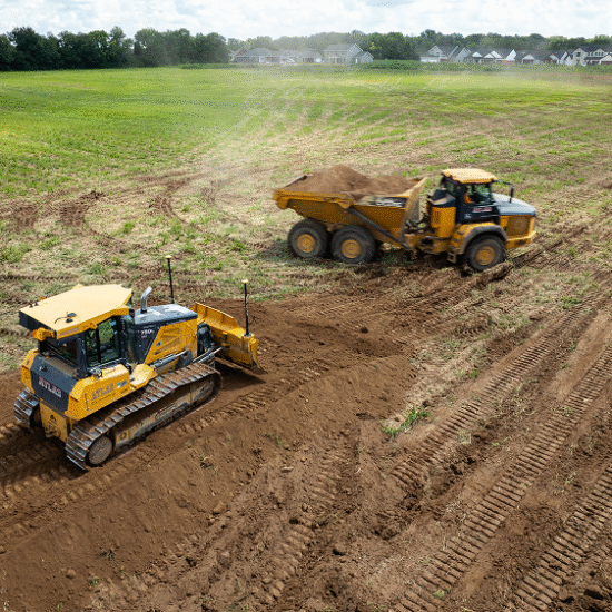 Bulldozer levels dirt as dump truck drives at construction site.