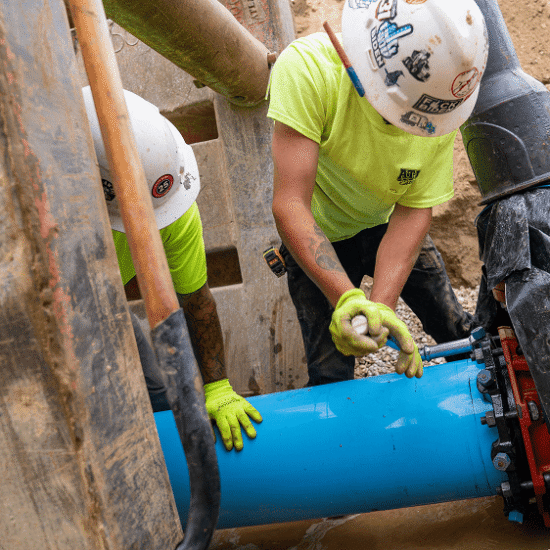 Two workers in hard hats install a large blue pipe.