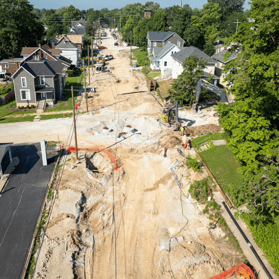 Residential street construction with dirt, equipment, barriers, and workers.