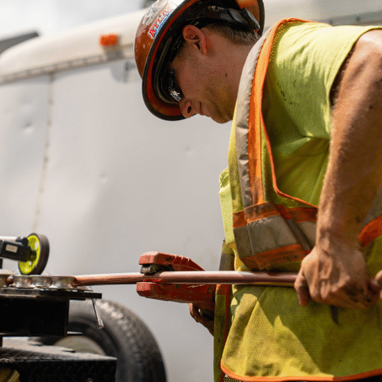 Worker in safety vest bends copper pipe outdoors.