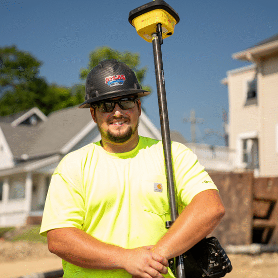 Worker in yellow shirt with hard hat holds survey rod outside.