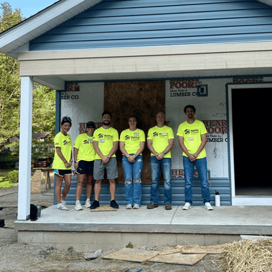 Six people in neon shirts on porch of blue house build.