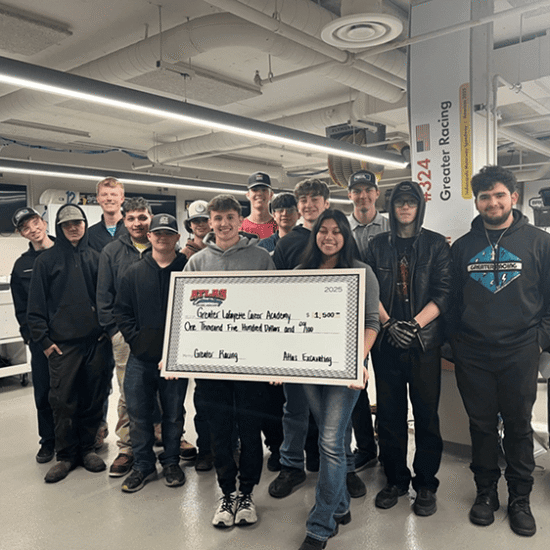 People hold $1,500 check indoors; auto equipment in background.