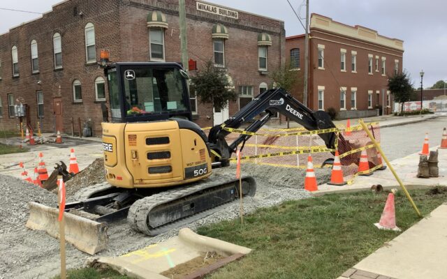 Small excavator at street site with cones, gravel, and tape.