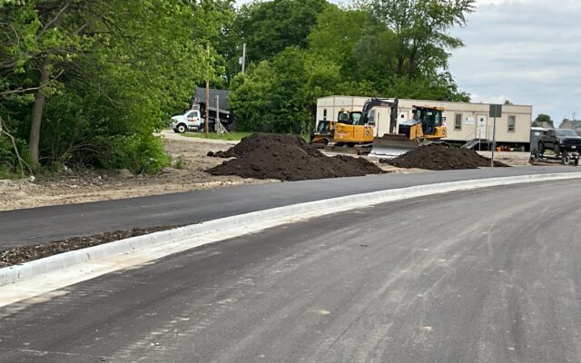 Newly paved road, curbs, dirt piles, equipment, trailers, trees.