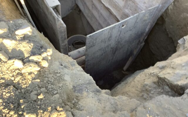 Trench with wood, metal walls and concrete pipe segment.