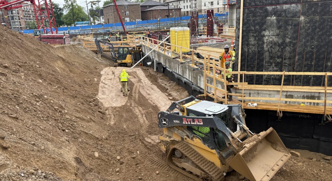 Workers and machinery at construction site under cloudy skies.