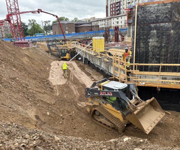 Workers and machinery at construction site under cloudy skies.