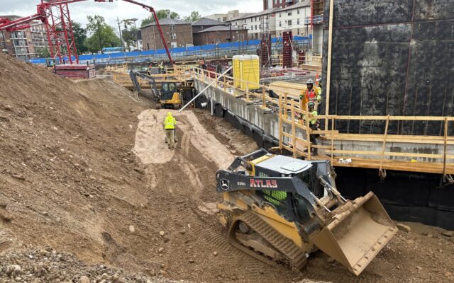 Workers and machinery at construction site under cloudy skies.