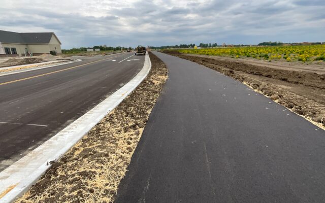 New asphalt bike path beside road, bare soil, cloudy sky.
