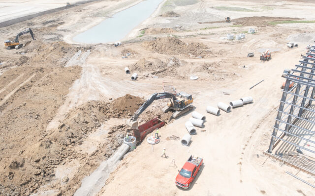 Aerial view: construction site, workers, machinery, red truck, pond.