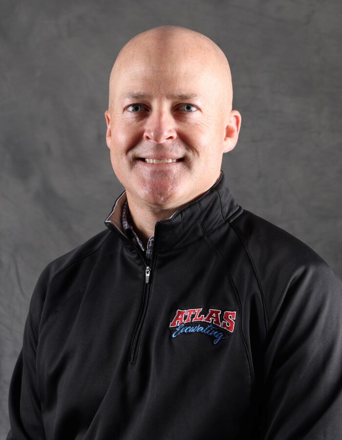 Smiling man in ATLAS jacket, gray backdrop.