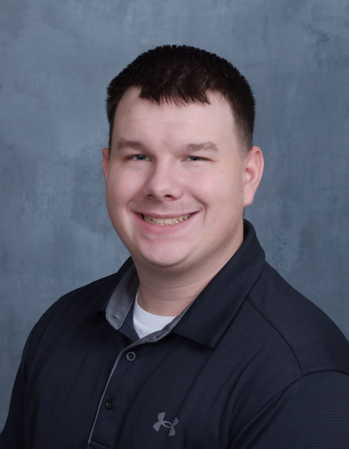 Man with short brown hair smiles in a dark collared shirt.