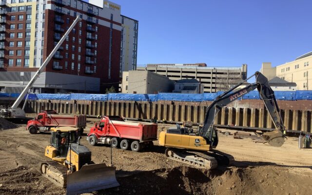 Excavators and trucks work at a sunny building site.