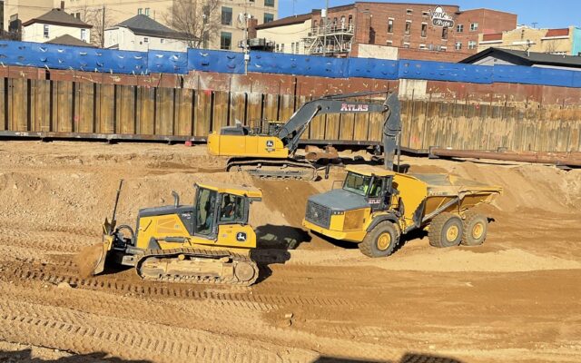 Three yellow construction vehicles work on a dirt site.