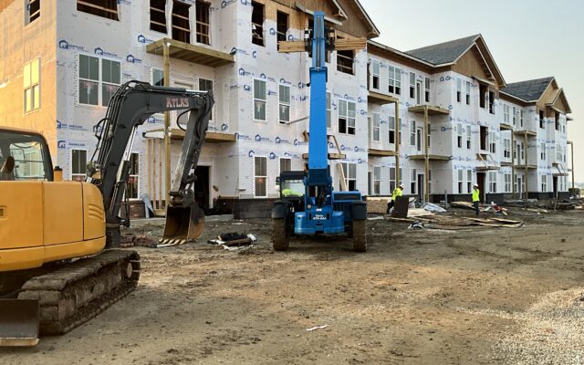 Unfinished apartments, blue lift, yellow excavator, workers present.