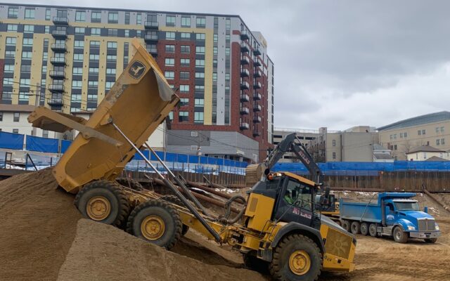 Yellow dump truck dumps dirt at construction site.