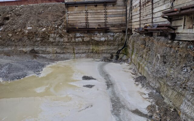 Excavation site with muddy water, soil layers, wooden walls.