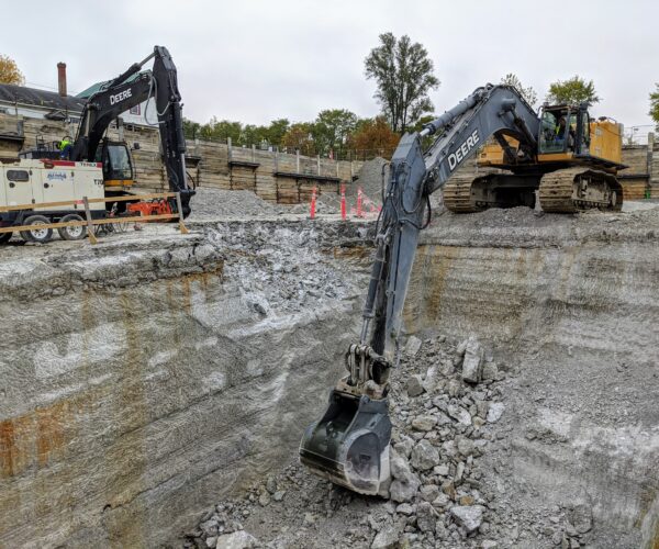 Two excavators operate at a construction site with rubble.