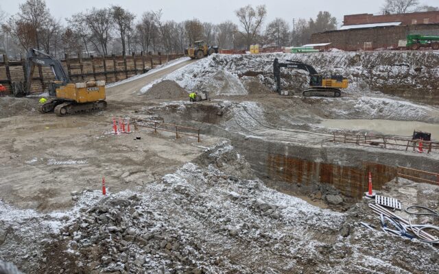 Excavators and workers at a snowy construction site.