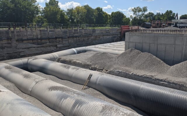 Construction site with covered pipes, gravel, concrete walls, dirt.