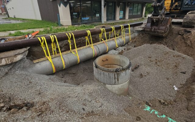 Construction site with pipes, manhole, excavator, and building.