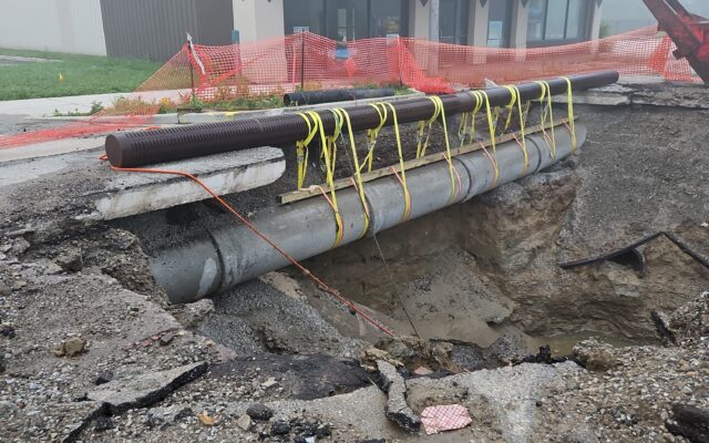 Road hole with pipes, rebar, barriers; foggy building behind.