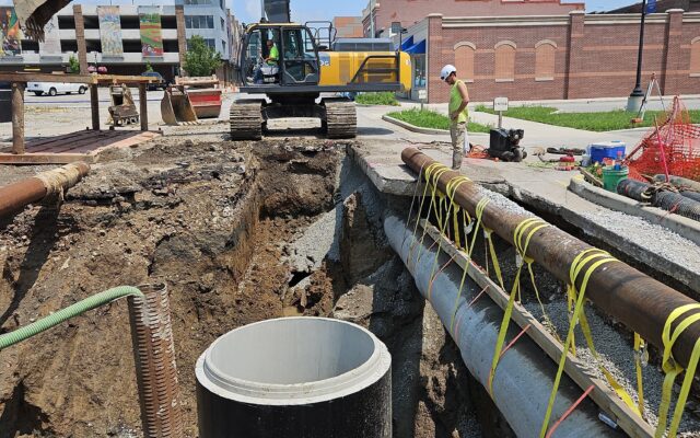 Excavator, workers, and pipes at city construction site.