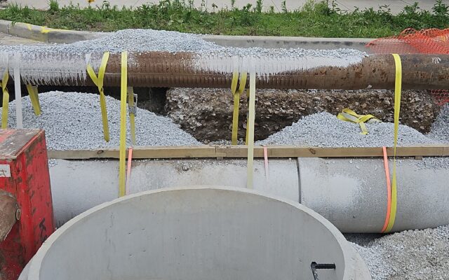 Concrete and metal pipes with yellow straps at construction site.