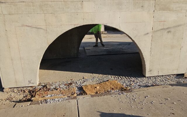 Two workers by concrete arch; shadow, timestamp in foreground.