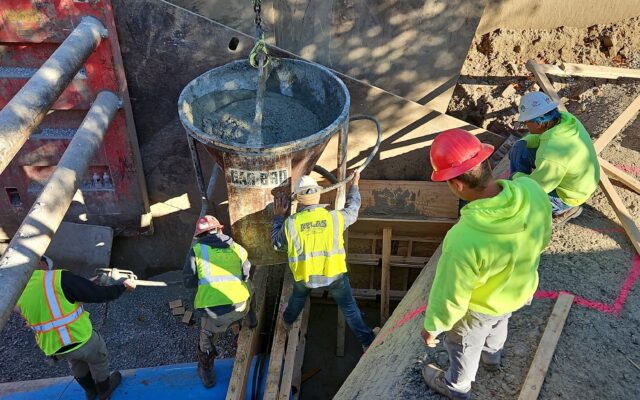 Workers pour concrete around a large blue pipe at site, 10/24/24.