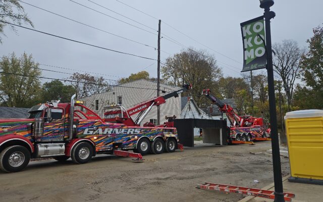 Tow trucks lift concrete structure near banner.