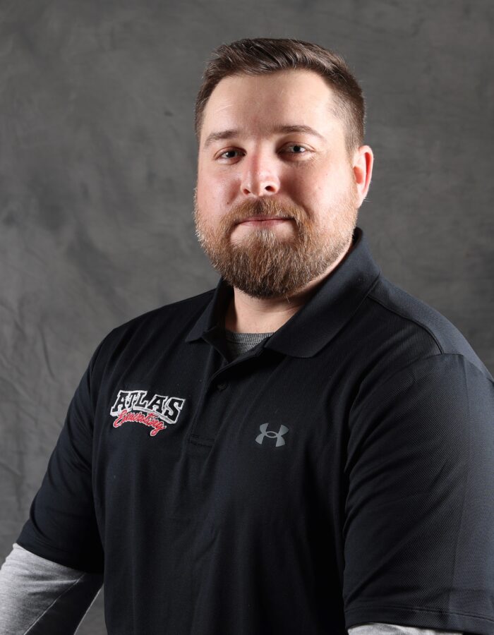 Bearded man in black "ATLAS" polo against gray backdrop.