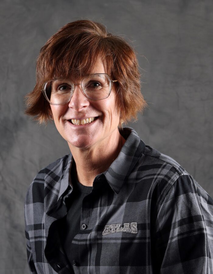 Smiling woman with short brown hair, glasses, and plaid shirt.