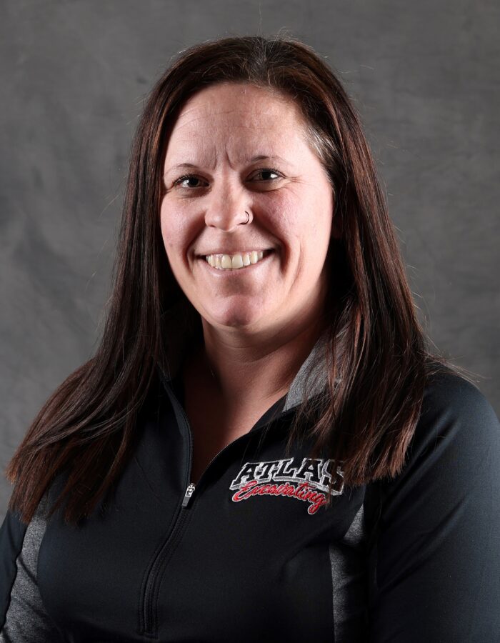 Woman with long brown hair smiles in black ATLAS top.
