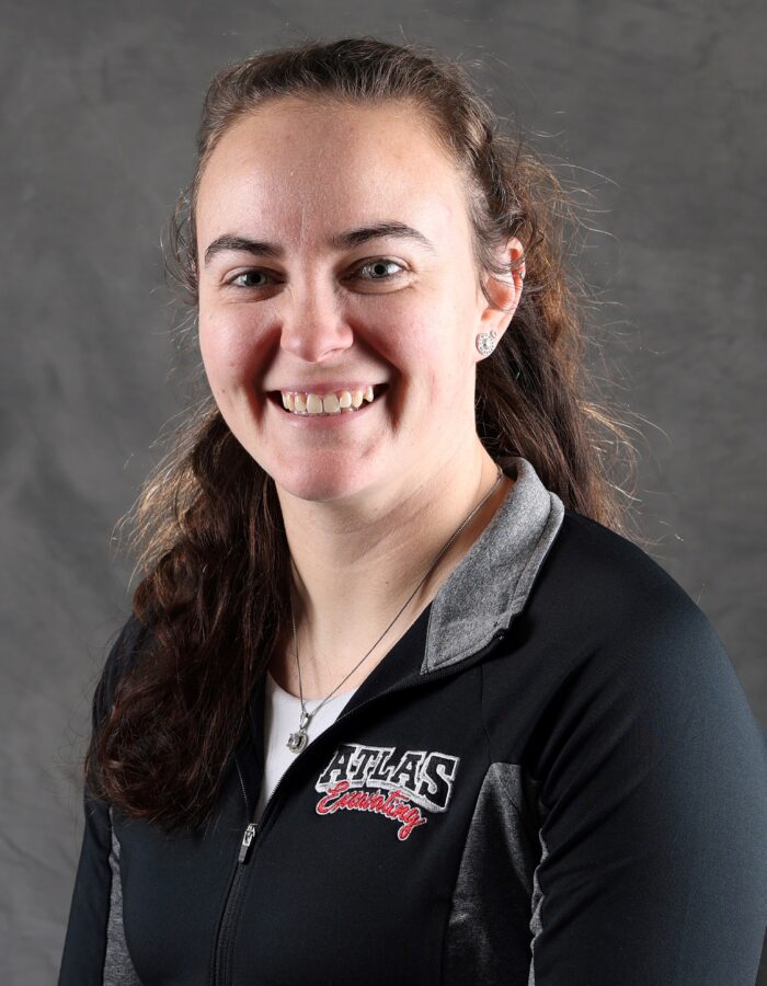 Smiling woman in ATLAS jacket, gray background.