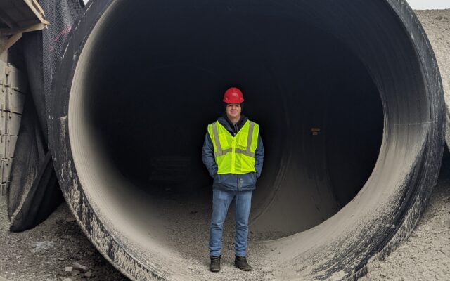 Person in red hard hat and yellow vest inside pipe.