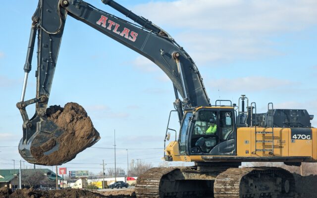 ATLAS excavator lifts dirt at construction site under clouds.