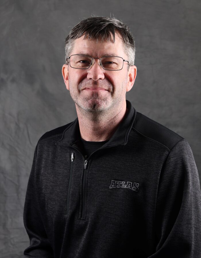 Man in glasses and ATLAS sweater before gray background.