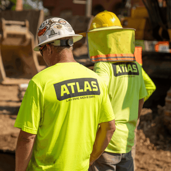 Two workers in yellow ATLAS shirts and hard hats at worksite.