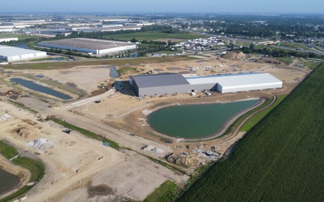 Industrial site with two big buildings, ponds, dirt, and greenery.