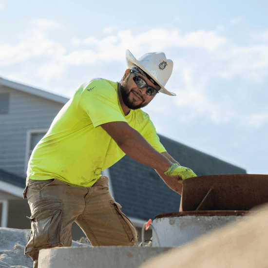 Man in cowboy hard hat and neon shirt works outside.