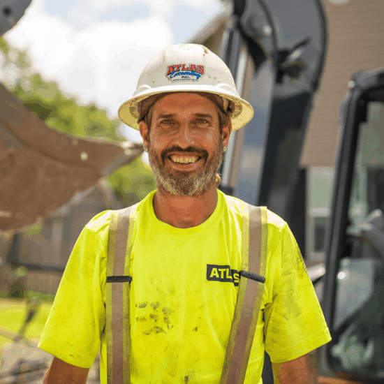 Smiling construction worker in yellow shirt, hard hat, outdoors.