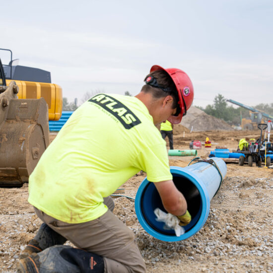 Worker in yellow shirt cleans inside large blue pipe outdoors.