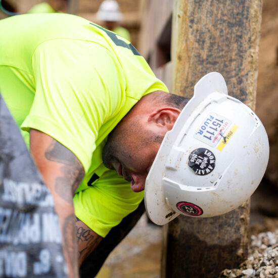 Worker in neon yellow, white hard hat, leans by metal beam.