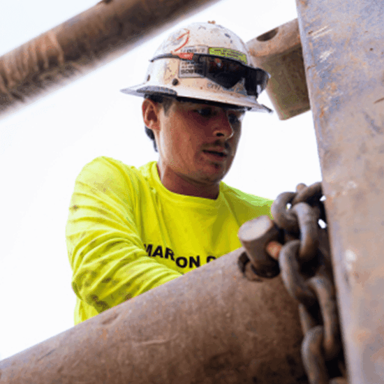 Worker in hard hat checks chains on metal beams.