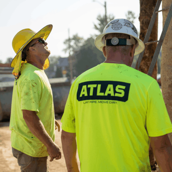 Two workers in yellow shirts and hard hats at worksite.